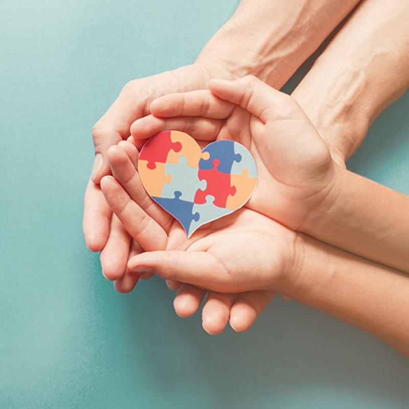 Adult and child hands holding a heart shaped jigsaw puzzle.