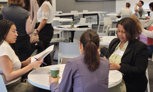Three women sit at a table chatting with each other.