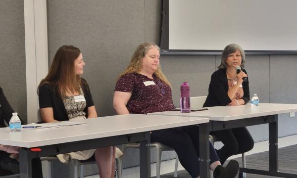 Four middle-aged white women sit at a table in front of CSUA conference attendees.