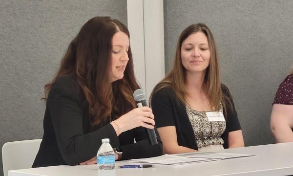 Four middle-aged white women sit at a table in front of CSUA conference attendees.
