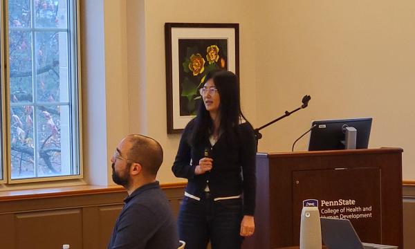 Xue Zhang, an Asian woman wearing a dark sweater, presents to the group. 