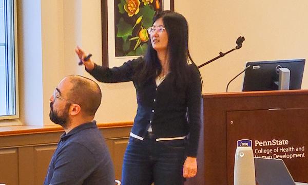 Xue Zhang, an Asian woman wearing a dark sweater, presents to the group. 