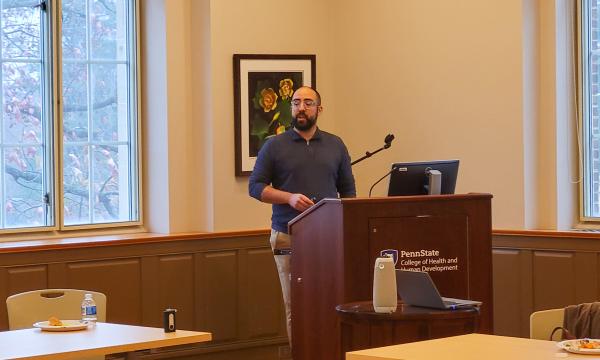 Nelson Roque, a white man wearing a blue shirt with a beard, presents to the group.