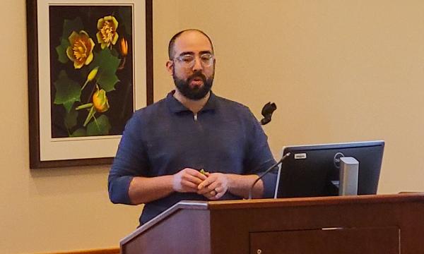 Nelson Roque, a white man wearing a blue shirt with a beard, presents to the group.