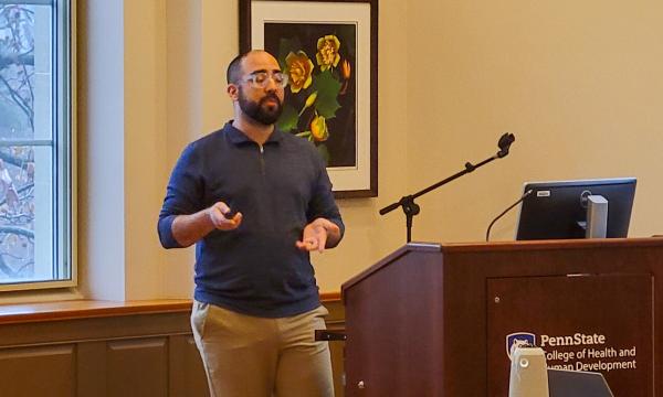 Nelson Roque, a faculty member wearing a blue shirt with a beard, holds a presentation clicker.
