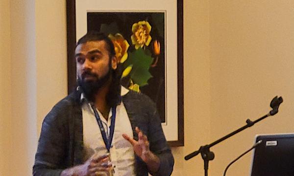 Mohanraj Krishnan, a faculty member wearing a long cardigan and white button-up, presents to the group.