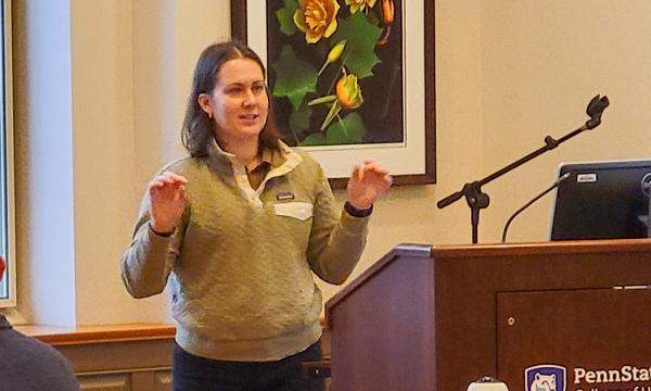 Tracee Saunders, a woman with shoulder-length brown hair wearing a green sweater, presents to the group.