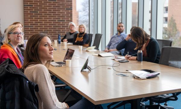 A group of PRI associates sit at a conference table and listen to a discussion.