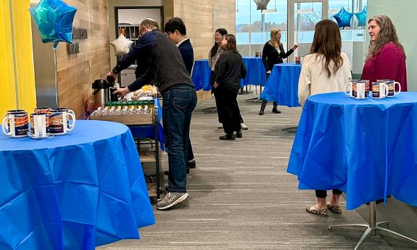 Attendees gathered around tables with blue tablecloths on them in the new Susan Welch Liberal Arts Building.