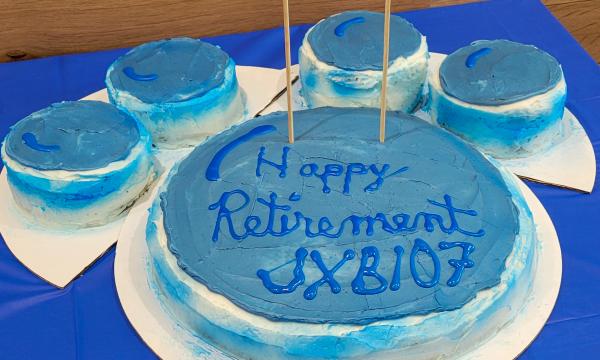 Pawprint shaped cake with blue and white frosting that says 'Happy Retirement JXB107."