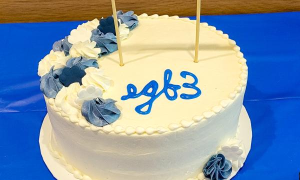 White cake with blue rosettes that says "egb3."