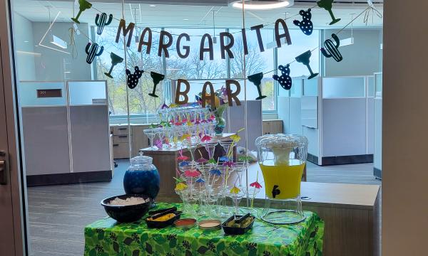 Green tablecloth covered table with a drinks station and a banner that says "Margarita Bar" on it.