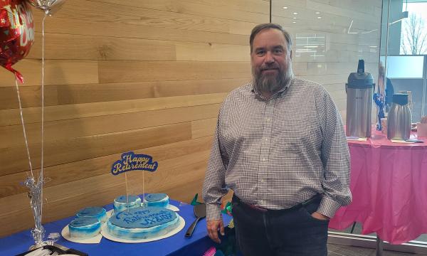 Joe Broniszewski, a middle-aged white man standing next to his retirement cake.