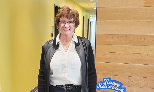 Betsy Beck, a middle-aged white woman in a black jacket standing next to her retirement cake.
