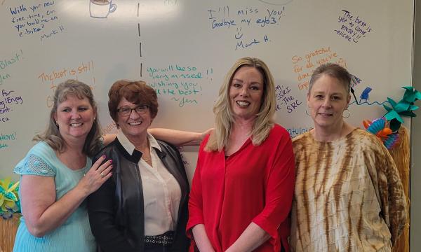 Group shot of four white women posed in front of a white board.
