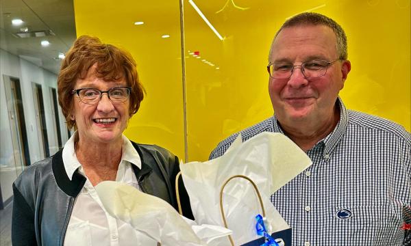 Betsy Beck and Joe Broniszewski stand at a table with their retirement gifts.